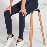 color=Indigo, Front angle, seated view of indigo toothpick denim jean leggings with patented concealed waistband